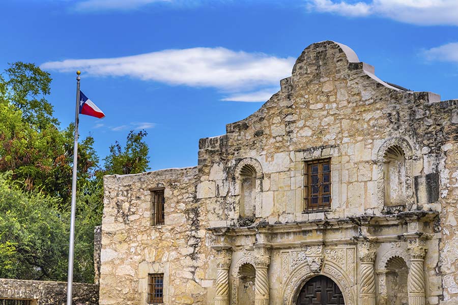 About Our Agency - Historical Alamo Building in San Antonio Texas Against a Bright Blue Sky with a Texas Flag Next to It