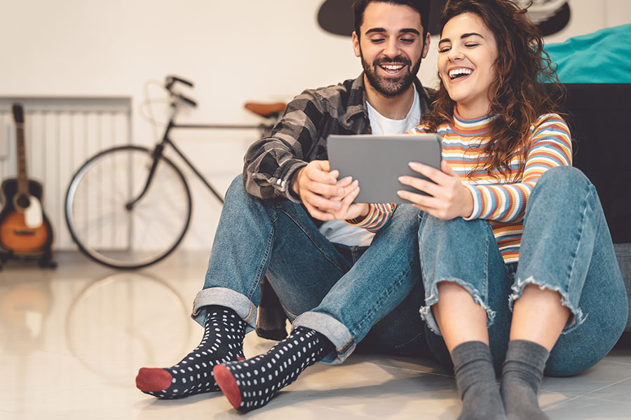 Personal Insurance - Portrait of a Cheerful Young Couple Sitting on the Floor in Their Apartment While Having Fun Watching Videos on a Tablet